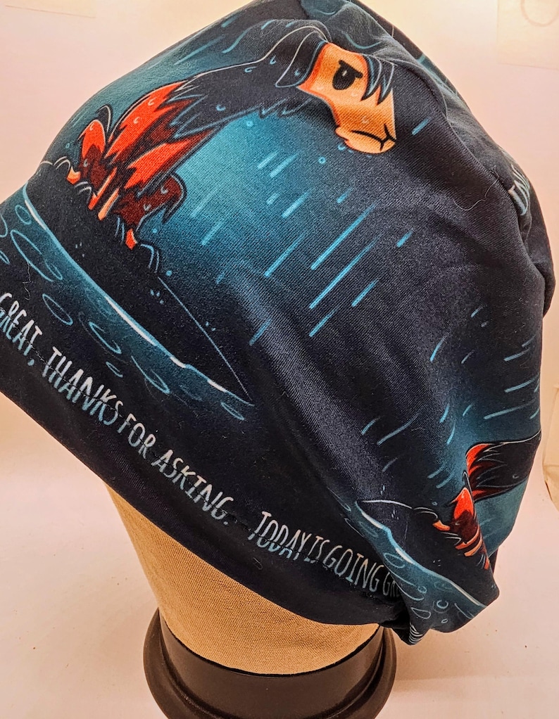 May include: A dark blue beanie with a cartoon dog design in orange, black, and white. The beanie has the text "GREAT, THANKS FOR ASKING. TODAY IS GOING" in white.