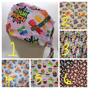 May include: A pink surgical scrub cap with a Sour Patch Kids candy pattern. The cap features the text "SOUR PATCH Kids" and "SOUR BUT SWEE" with colorful candy graphics. The cap is tied at the back.