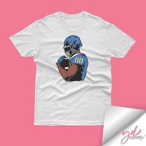 May include: White t-shirt with a graphic of a football player wearing a blue helmet and jersey with the number "00" on it.