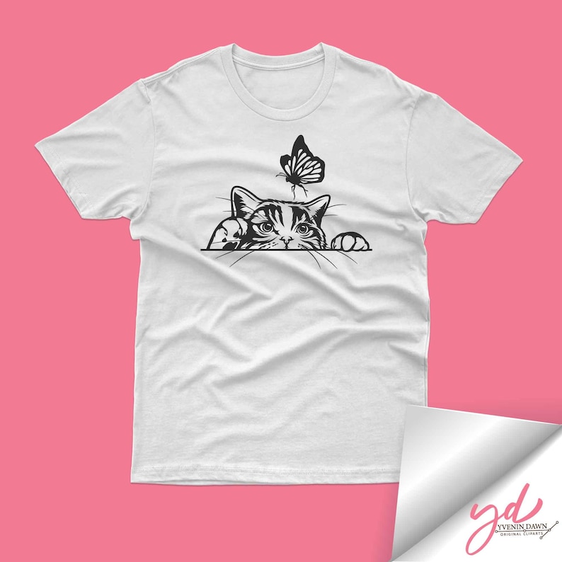 Pode incluir: Uma camiseta branca com uma ilustra&ccedil;&atilde;o em preto e branco de um gato espiando por tr&aacute;s de uma superf&iacute;cie com uma borboleta acima.