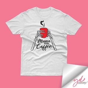 May include: White t-shirt with a black skeleton hand holding a red coffee mug. The text "Mama Needs Coffee" is printed on the shirt.