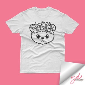 May include: White t-shirt with a black and white illustration of a bear wearing a flower crown.