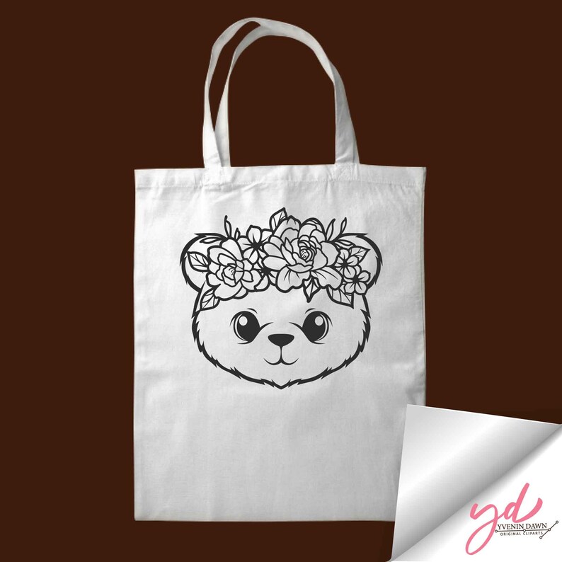 May include: A white tote bag with a black and white illustration of a bear wearing a flower crown. The bear has large eyes and a cute expression.
