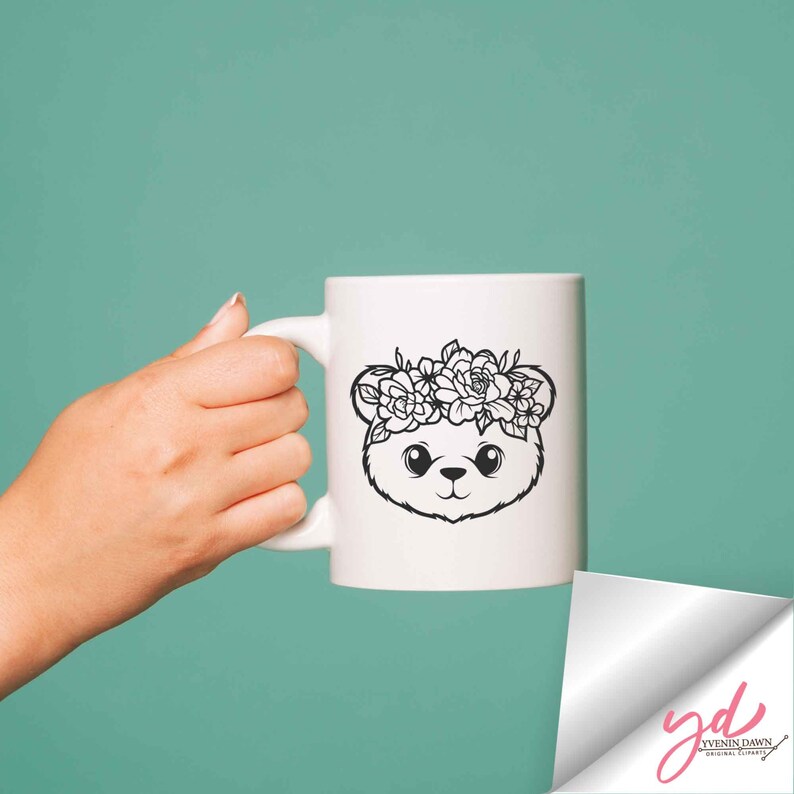 May include: White ceramic mug with a black line drawing of a bear wearing a flower crown. The bear has large eyes and a small nose.
