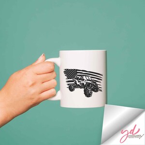 May include: White ceramic mug with a black and white image of an off-road vehicle driving over a tattered American flag.