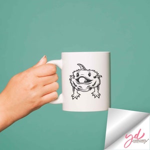 Puede incluir: Taza de cer&aacute;mica blanca con una ilustraci&oacute;n en blanco y negro de un drag&oacute;n barbudo en la parte delantera. El drag&oacute;n est&aacute; sonriendo y tiene una cresta puntiaguda en la cabeza.