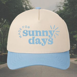 May include: A beige and light blue baseball cap with the text "Made for sunny days" in blue lettering.