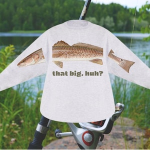 May include: A light gray long-sleeve shirt featuring a detailed illustration of a fish, with the text "that big, huh?" in a dark green color. The fish illustration is in shades of brown and tan. Fishing-themed apparel.