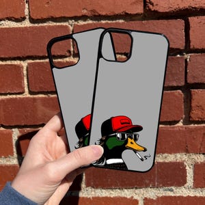 Pu&ograve; includere: Due custodie per telefono grigie con bordo nero. Le custodie presentano un'illustrazione di un cartone animato di un'anatra con occhiali da sole, un berretto da baseball rosso e che fuma una sigaretta.