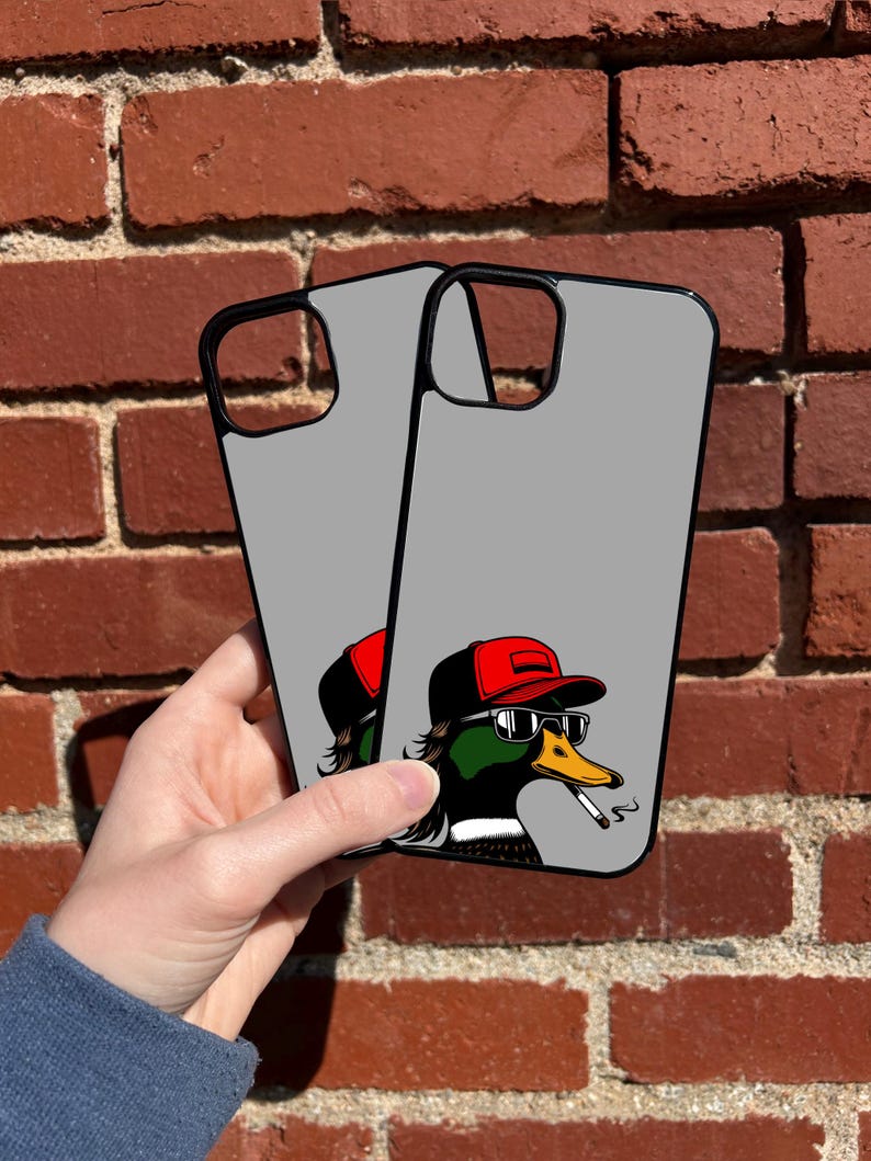 Pu&ograve; includere: Due custodie per telefono grigie con bordo nero. Le custodie presentano un'illustrazione di un cartone animato di un'anatra con occhiali da sole, un berretto da baseball rosso e che fuma una sigaretta.