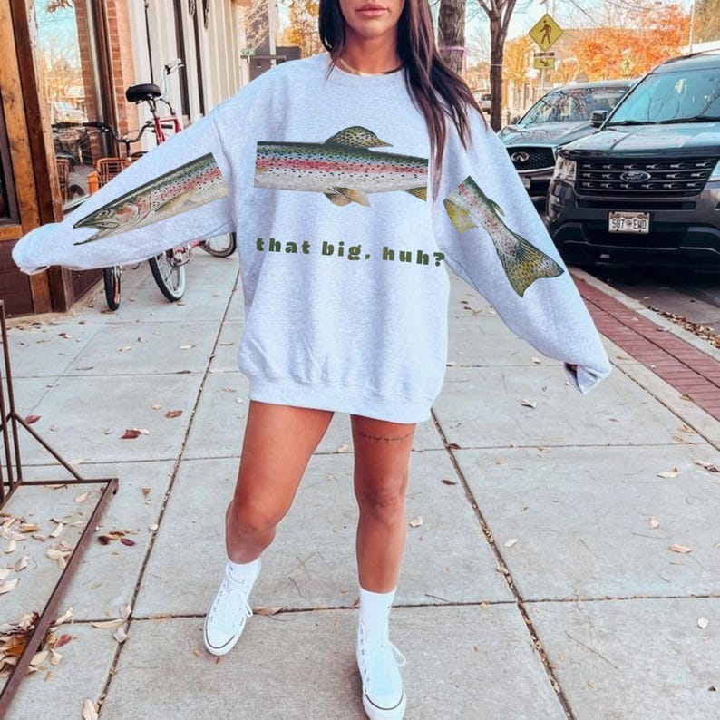 May include: Light gray sweatshirt with a fish graphic on the front and sleeves. The fish is a rainbow trout with red, green, and yellow markings. The text "that big, huh?" is printed below the fish.