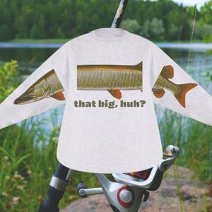 May include: A light gray long-sleeve shirt featuring a fish illustration. The shirt has a fish head on one sleeve, a fish body on the front, and a fish tail on the other sleeve. The text "that big, huh?" is printed on the front.