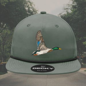 May include: A green baseball cap with a black brim and a black band around the crown. The cap has an embroidered image of a duck in flight and the text "DECKY ORIGINAL" on the front.