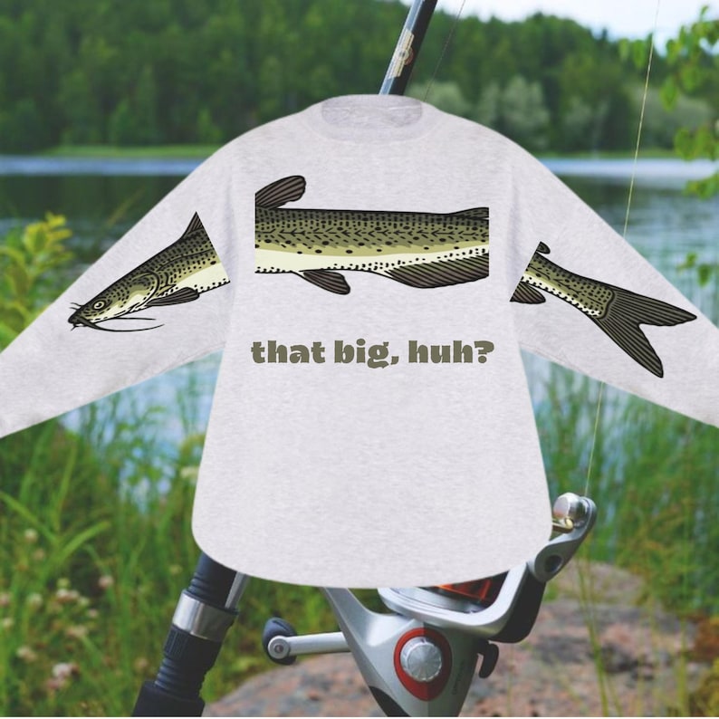 May include: A light gray long-sleeve shirt featuring a fish design on the sleeves and torso. The fish is depicted in shades of green, brown, and black. The text "that big, huh?" is printed below the fish graphic.