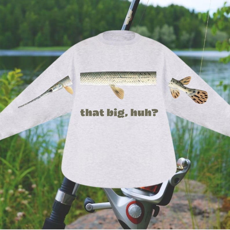 May include: A light gray long-sleeve shirt with a fish design. The shirt features a fish scale pattern and the text "that big, huh?" in a dark green color. The design includes fish parts on the sleeves.