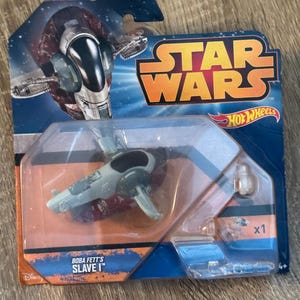 May include: A Star Wars Hot Wheels toy car in its original packaging. The packaging is blue and orange with the Star Wars logo and the words "Boba Fett's Slave I". The toy car is gray and black.