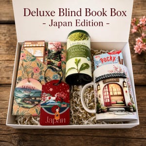 May include: A white gift box labeled Deluxe Blind Book Box - Japan Edition containing a Republic of Tea Double Green Matcha tin, a Pocky box, a mug with an onsen illustration, a Japan 2026 ornament, a Japan luggage tag, and a floral book sleeve.