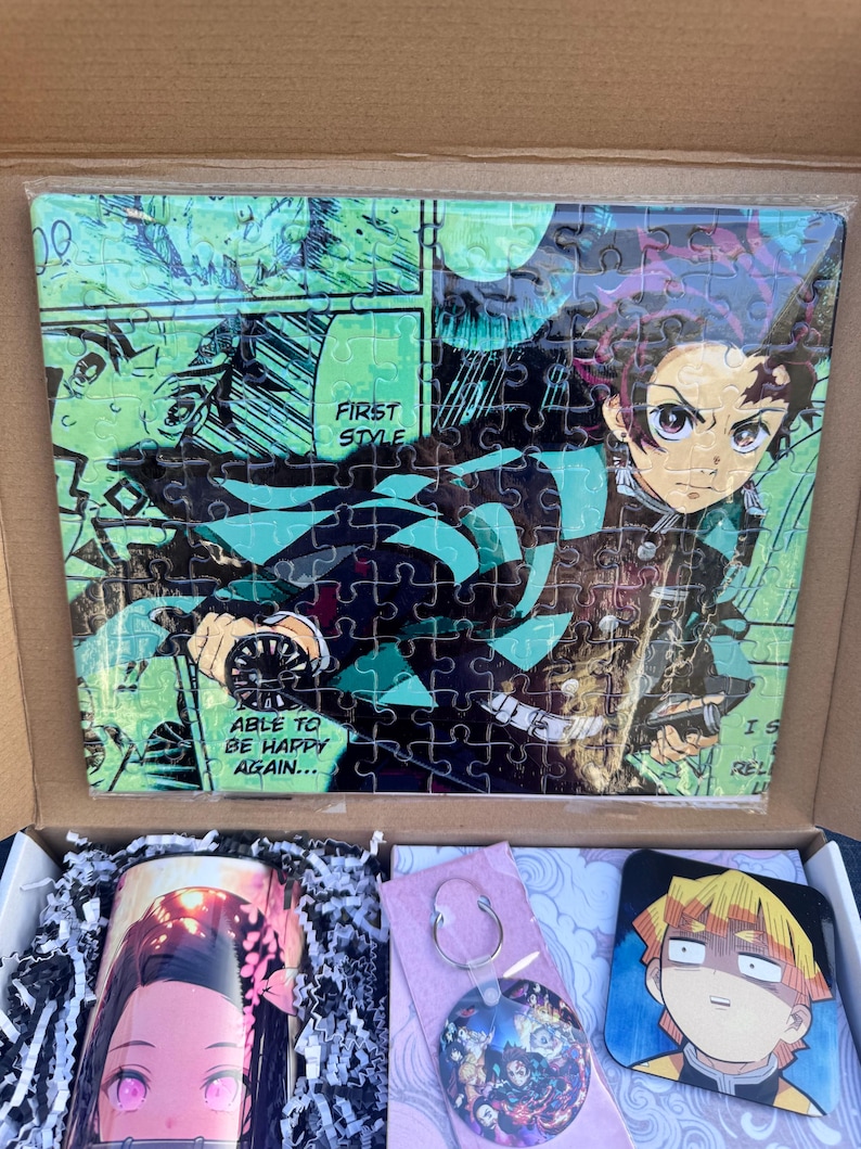 May include: A gift box set featuring a Demon Slayer anime puzzle, a mug with a character from the anime, a keychain with a round anime character charm, and a square coaster with a different anime character. The puzzle features a green and black background with a character holding a sword. The mug features a pink and white character with pink eyes. The keychain features a round charm with multiple anime characters. The coaster features a yellow and black character with a surprised expression.