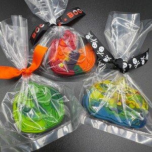 K&ouml;nnte beinhalten: Drei einzeln verpackte Halloween-Wachs-Schmelzen. Die Schmelzen sind in Form von K&uuml;rbissen und haben ein Batik-Design. Die erste Schmelze ist rot, orange und lila. Die zweite Schmelze ist gr&uuml;n und gelb. Die dritte Schmelze ist blau und gelb.