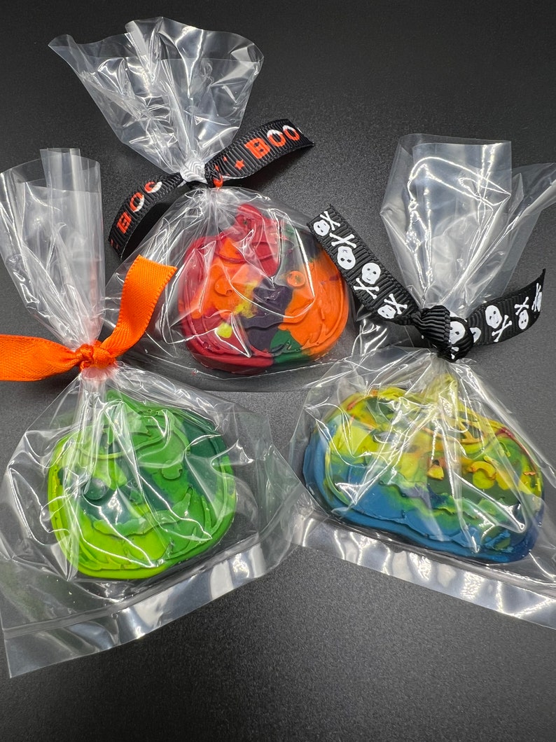 K&ouml;nnte beinhalten: Drei einzeln verpackte Halloween-Wachs-Schmelzen. Die Schmelzen sind in Form von K&uuml;rbissen und haben ein Batik-Design. Die erste Schmelze ist rot, orange und lila. Die zweite Schmelze ist gr&uuml;n und gelb. Die dritte Schmelze ist blau und gelb.