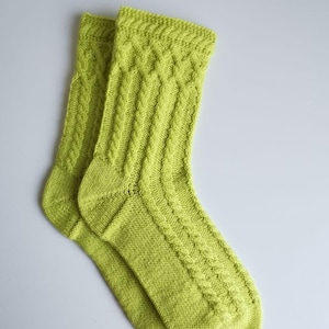 Pode incluir: Um par de meias de lã verde limão com um padrão de trança.