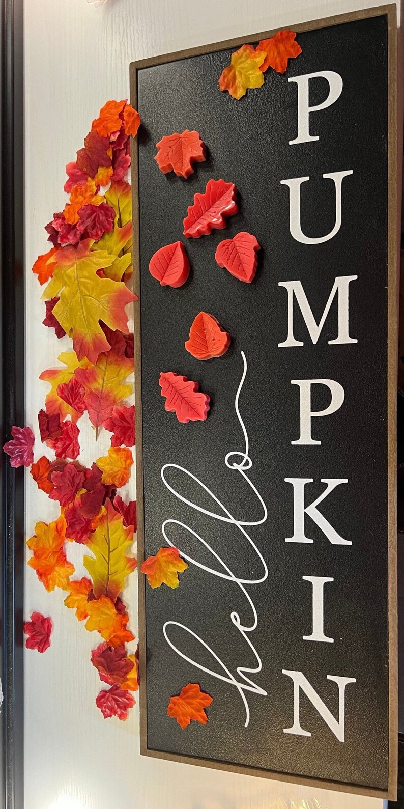 May include: A black sign with the word "Pumpkin" written in white letters. The sign is decorated with red fall leaves. The word "Hello" is written in white cursive on the sign.