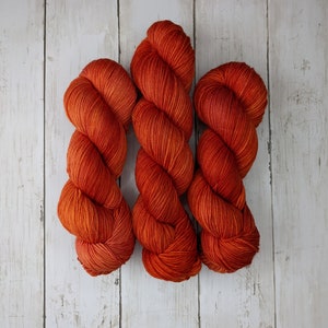 May include: Three skeins of orange yarn, each wound into a ball shape. The yarn is a deep orange color with a slight reddish hue.