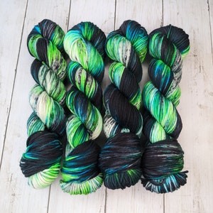 May include: Four skeins of yarn in a black, green, and blue colorway. The yarn is arranged in a row, with the ends of each skein overlapping.