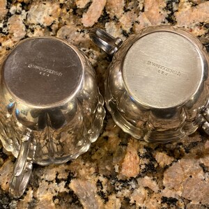 May include: Bottom view of two silver creamer and sugar bowls with the inscription "1847 Rogers Bros." and "624" on the bottom.