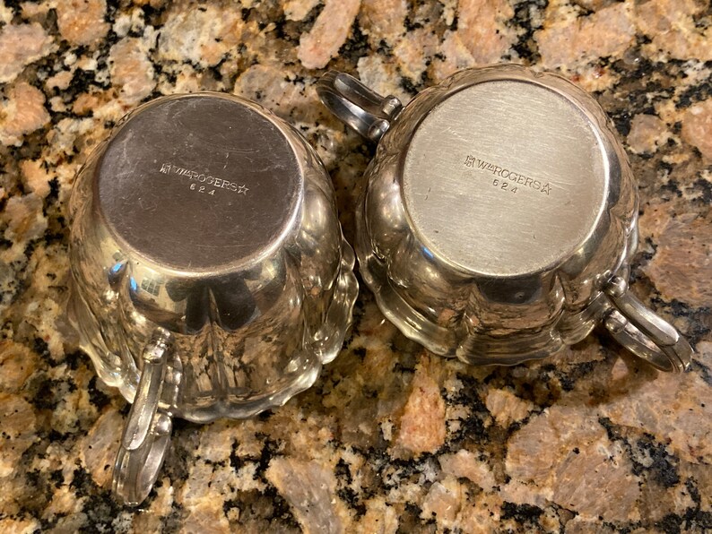 May include: Bottom view of two silver creamer and sugar bowls with the inscription "1847 Rogers Bros." and "624" on the bottom.