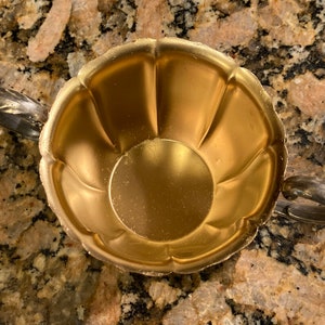 May include: A gold-colored metal sugar bowl with two handles. The bowl has a fluted design and a smooth, shiny finish.