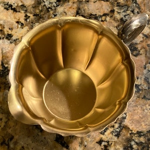 May include: A gold-colored metal creamer with a fluted design and a silver handle.