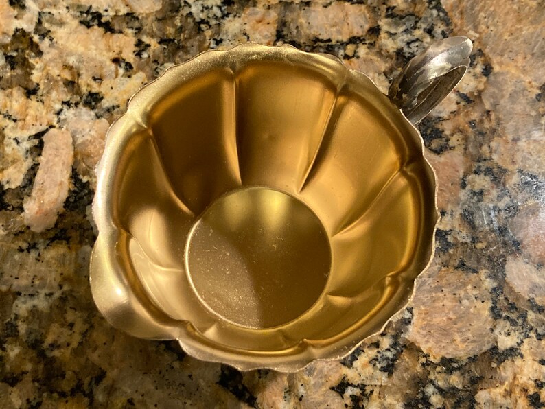 May include: A gold-colored metal creamer with a fluted design and a silver handle.