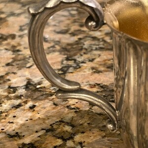 May include: A silver sugar bowl with a decorative handle. The bowl has a fluted design and is made of metal.