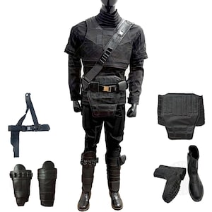 Può includere: Set di costume nero e grigio con gilet, pantaloni, stivali e accessori. Il gilet ha una cinghia nera e una cintura con una fibbia dorata. Gli stivali hanno cinturini e fibbie nere. Gli accessori includono una cintura, un paio di protezioni per le gambe e un pezzo posteriore.