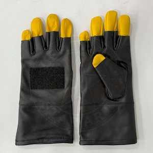 May include: A pair of black leather gloves with yellow fingertips. The gloves have a hook and loop patch on the back of the hand. The gloves are designed for protection and durability.