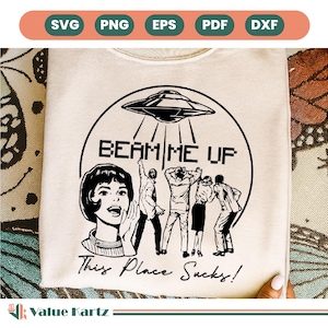 May include: Cream-colored sweatshirt with a black graphic of a UFO beaming up a group of people. Text reads "BEAM ME UP" and "This Place Sucks!" A retro-style woman is also featured in the design. The top is a unique statement piece.