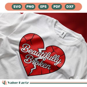 May include: White sweatshirt featuring a large, cracked red heart graphic with the words "Beautifully Broken" in white script. The design is centered on the chest of the shirt. The shirt has a simple, crew neck design.