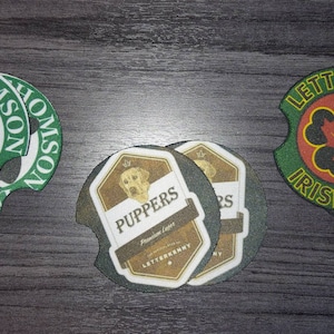 May include: Set of three car coasters with unique designs. One features a cow and the text "Dicky Thomson Dairy", another has a dog and the text "PUPPERS", and the last one has a maple leaf and the text "LETTERKENNY IRISH".