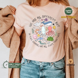 May include: A pink t-shirt with a circle design featuring various sea creatures and the text "We are all different but in this school we all swim together."