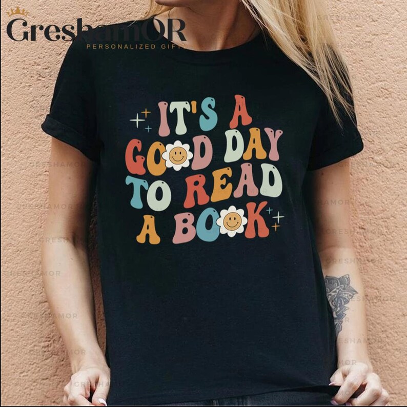 Pode incluir: Camiseta preta com um gr&aacute;fico retro colorido que diz "It's a good day to read a book" com um design de flor sorridente.