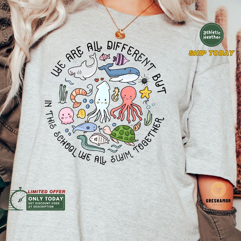 May include: A light gray t-shirt with a circle graphic of various sea creatures, including a turtle, octopus, fish, and a shark. The text "We are all different but in this school we all swim together" is written around the circle graphic.