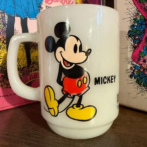 Pu&ograve; includere: Tazza in ceramica bianca con un'immagine colorata di Topolino. Topolino &egrave; raffigurato nel suo abito classico con pantaloncini rossi, scarpe gialle e guanti neri. La parola "MICKEY" &egrave; stampata in nero sulla tazza.