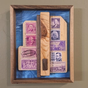 May include: Framed artwork featuring vintage postage stamps in shades of purple and brown. The stamps depict portraits and historical scenes, mounted on a wooden backing with a blue background. The frame is made of wood.