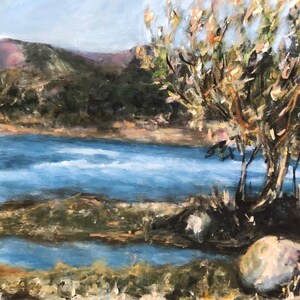 May include: A painting depicting a blue lake with a mountain range in the background. The lake is surrounded by trees and bushes. There is a large rock in the foreground.