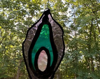 Puede incluir: Una ventana de vitral colgante con un diseño en turquesa, morado y blanco. La ventana tiene forma de lágrima y tiene un contorno negro.