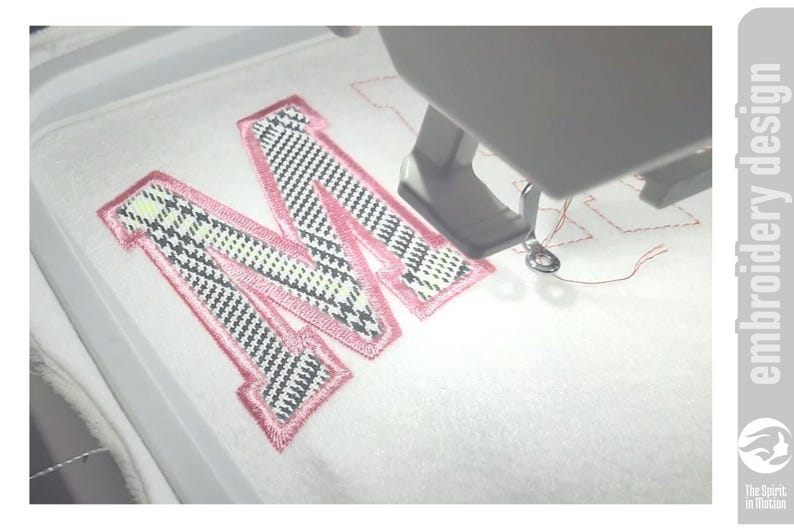 May include: An embroidery machine stitching a pink-outlined letter "M" onto white fabric. The letter has a black, white, and light green plaid pattern. The text "embroidery design" is on the right side of the image.