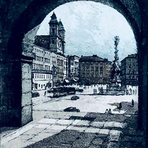 May include: A framed monochromatic etching depicting a city square viewed through a stone archway. The scene features multi-story buildings, a central monument, and a lantern hanging from the arch. The artwork is signed in the bottom right corner.