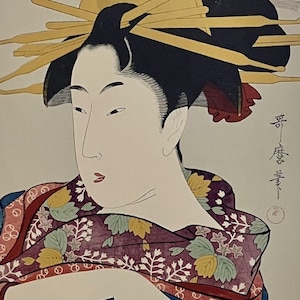 Puede incluir: Una impresión japonesa tradicional en madera que representa a una mujer con un kimono colorido con un patrón floral. Su cabello está peinado con un moño negro y adornado con palos dorados. La impresión está firmada en caracteres japoneses.