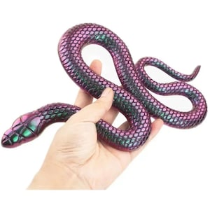Peut inclure: Un jouet serpent en caoutchouc avec des écailles irisées violettes et vertes. Le serpent est enroulé dans une pose réaliste.